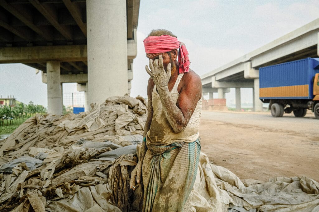 Dust-covered construction worker wiping his face beneath elevated flyovers in Ashulia, Dhaka.